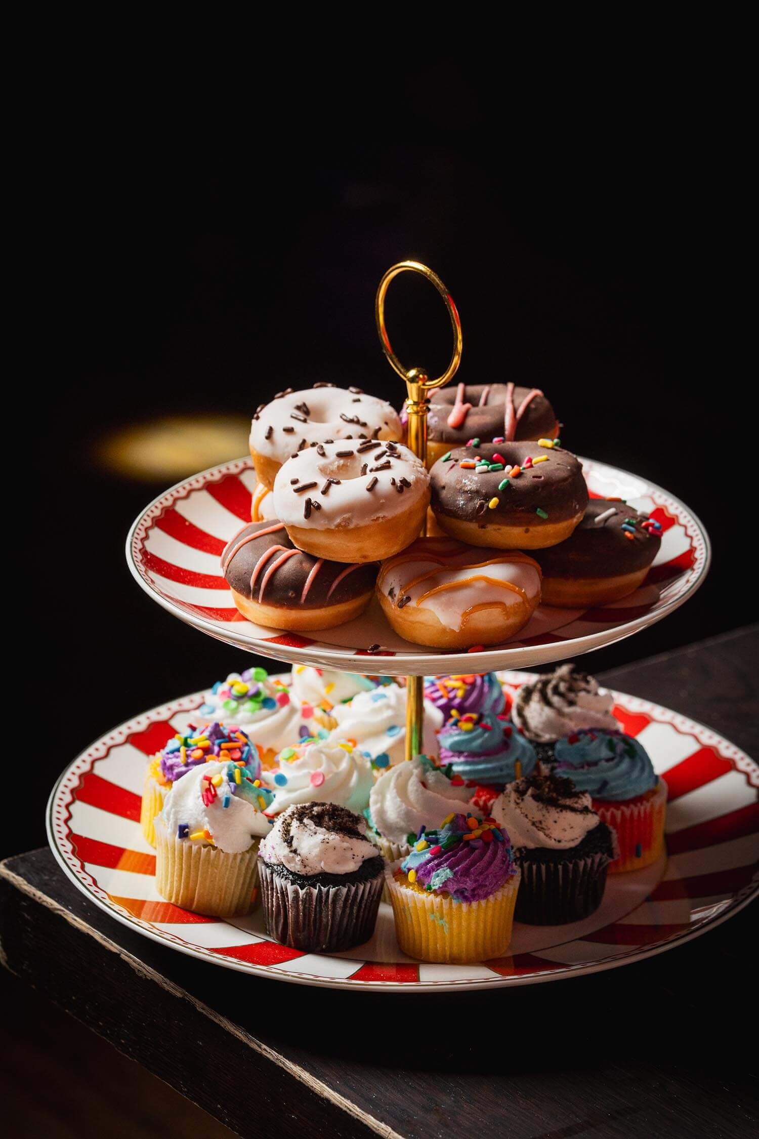 Two-tiered serving tray with assorted donuts on the top tier and colorful frosted cupcakes on the bottom tier.