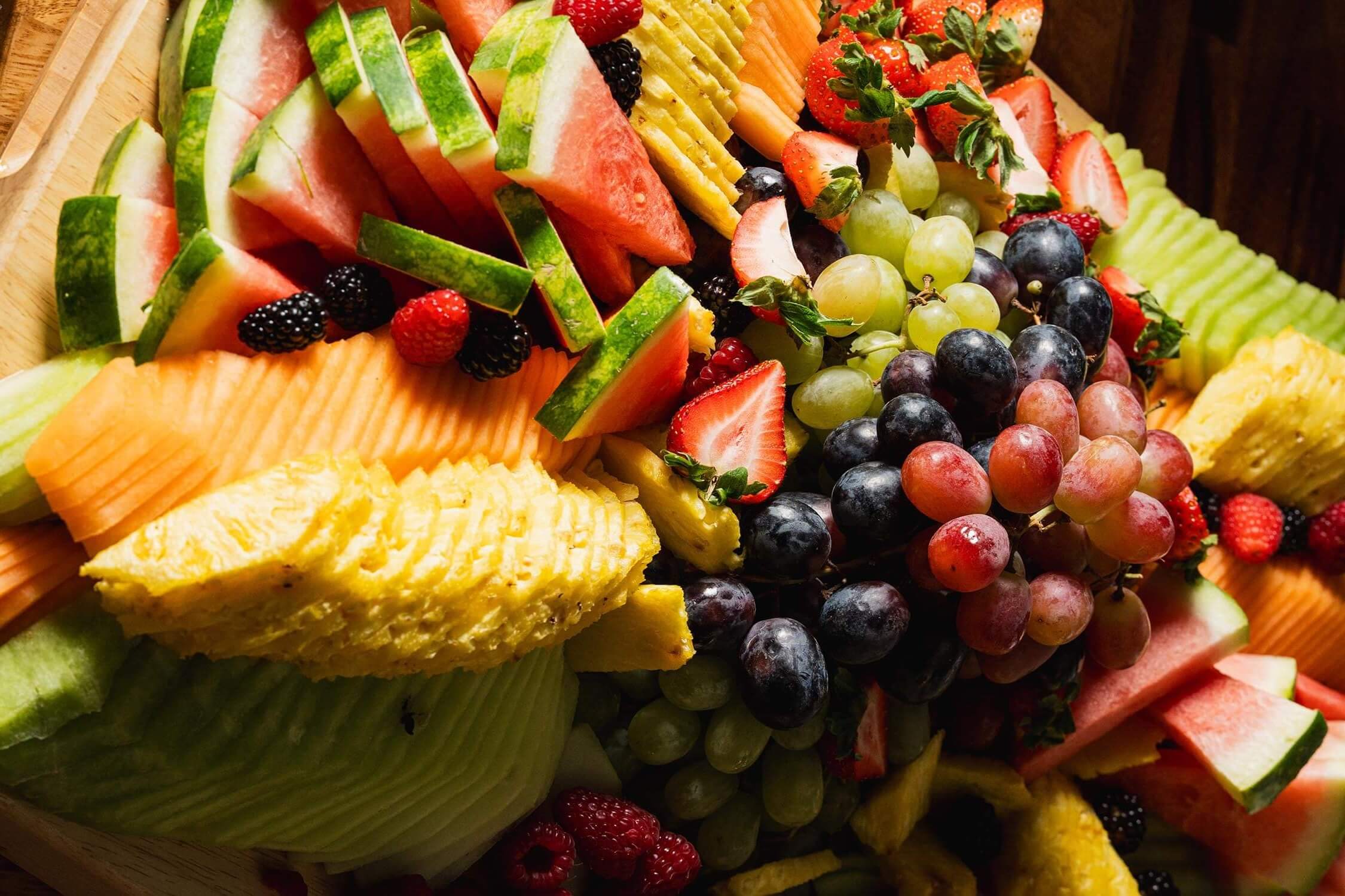 Assorted fresh fruit platter with sliced watermelon, pineapple, cantaloupe, honeydew, strawberries, grapes, raspberries, and blackberries.