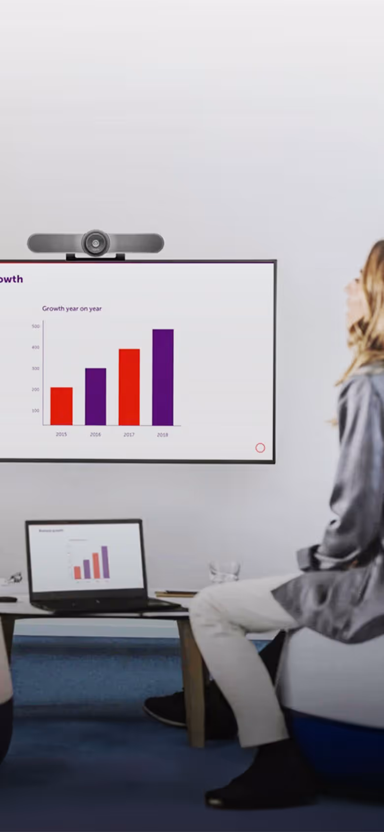 Casual business meeting in office with a wall-mounted TV and camera and laptop on small table