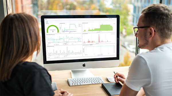Man and woman sitting together in front of desktop monitor reviewing complex data dashboards on screen