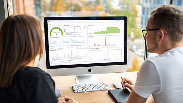 Man and woman sitting together in front of desktop monitor reviewing complex data dashboards on screen
