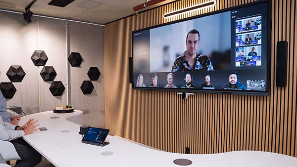 Signature Microsoft Teams Room with large wide-format display, wall-mounted speakers in front of modern curved meeting table.