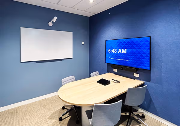 Microsoft Teams Rooms Small Room with a small huddle desk, four office chairs, wall-mounted display and whiteboard.