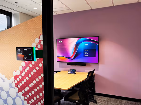 Small meeting room with wall-mounted display in front of a small desk and office chairs