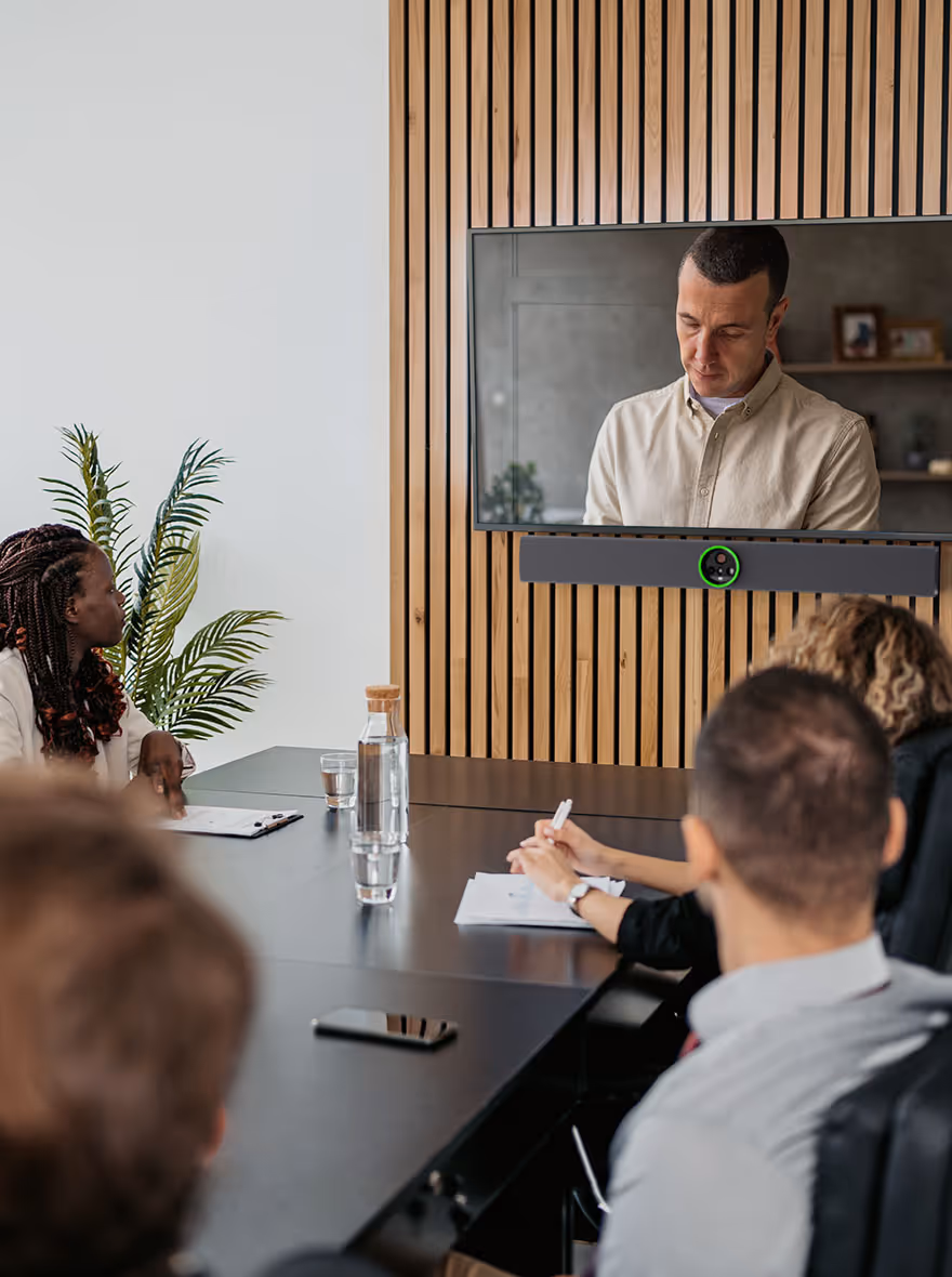 A man speaking on a video call displayed on a wall-mounted TV with Crestron Videobar.