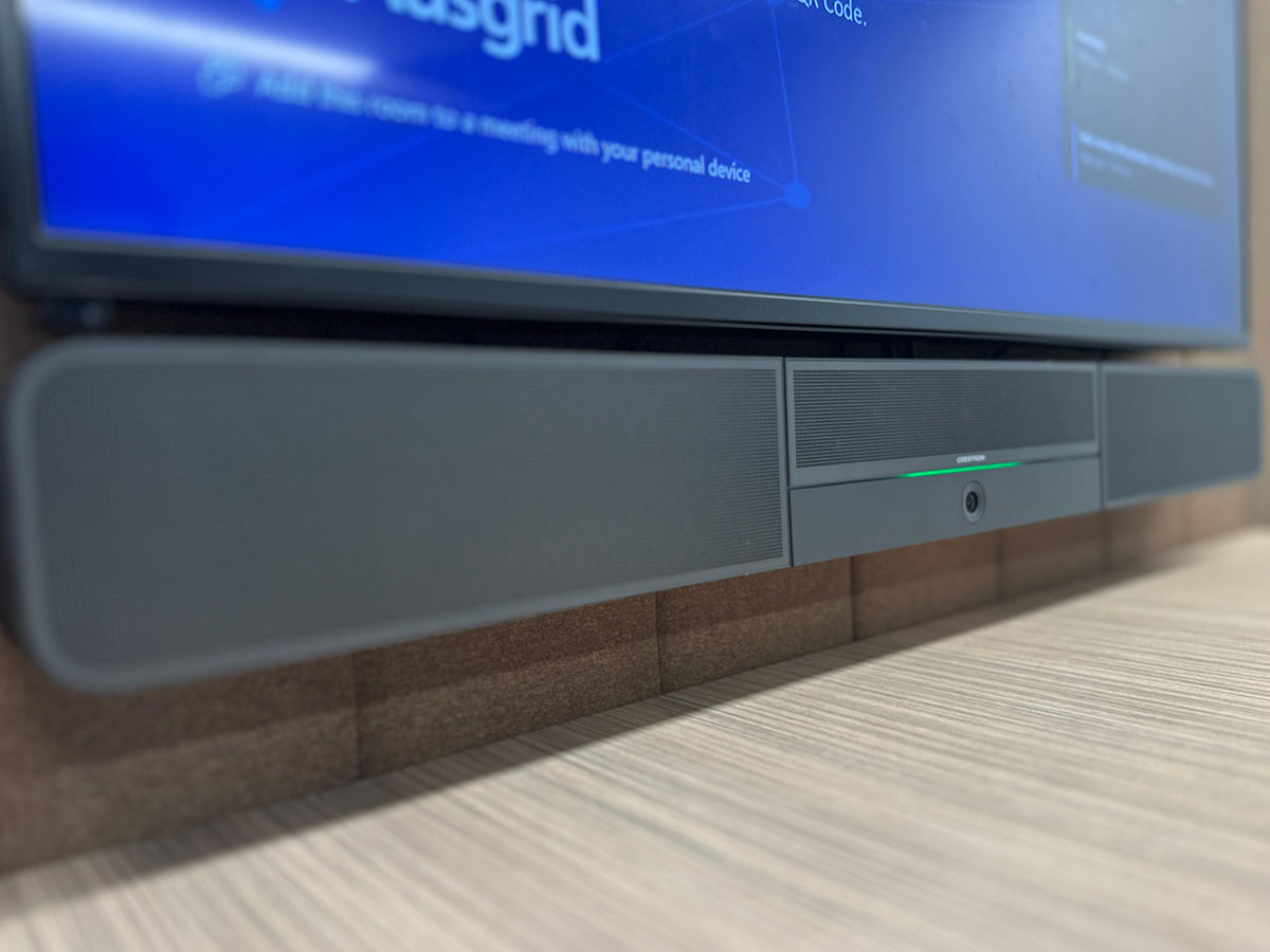 Close-up of a Crestron soundbar installed below a large wall-mounted display in a meeting room.