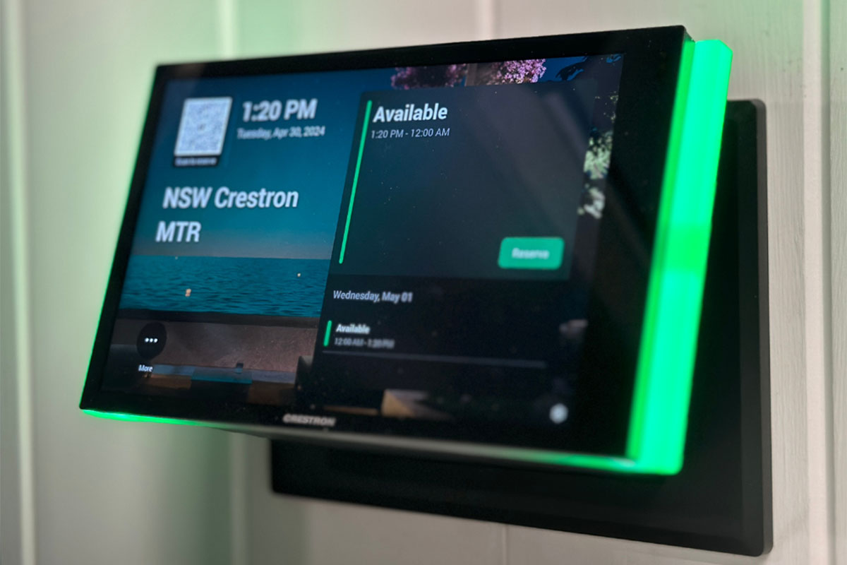 Wall-mounted Crestron touchscreen panel with green light indicating room availability in an office.