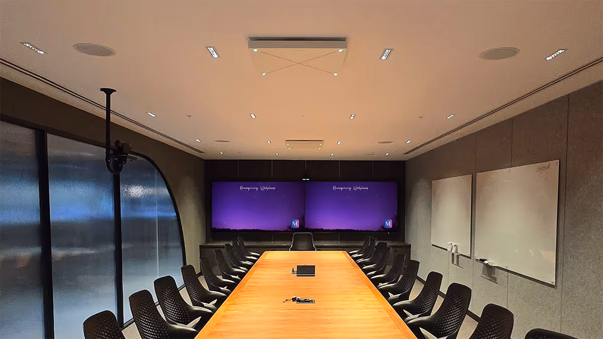 Modern boardroom with long wooden table, black chairs, two large screens displaying purple Merge background, and whiteboards on the wall.