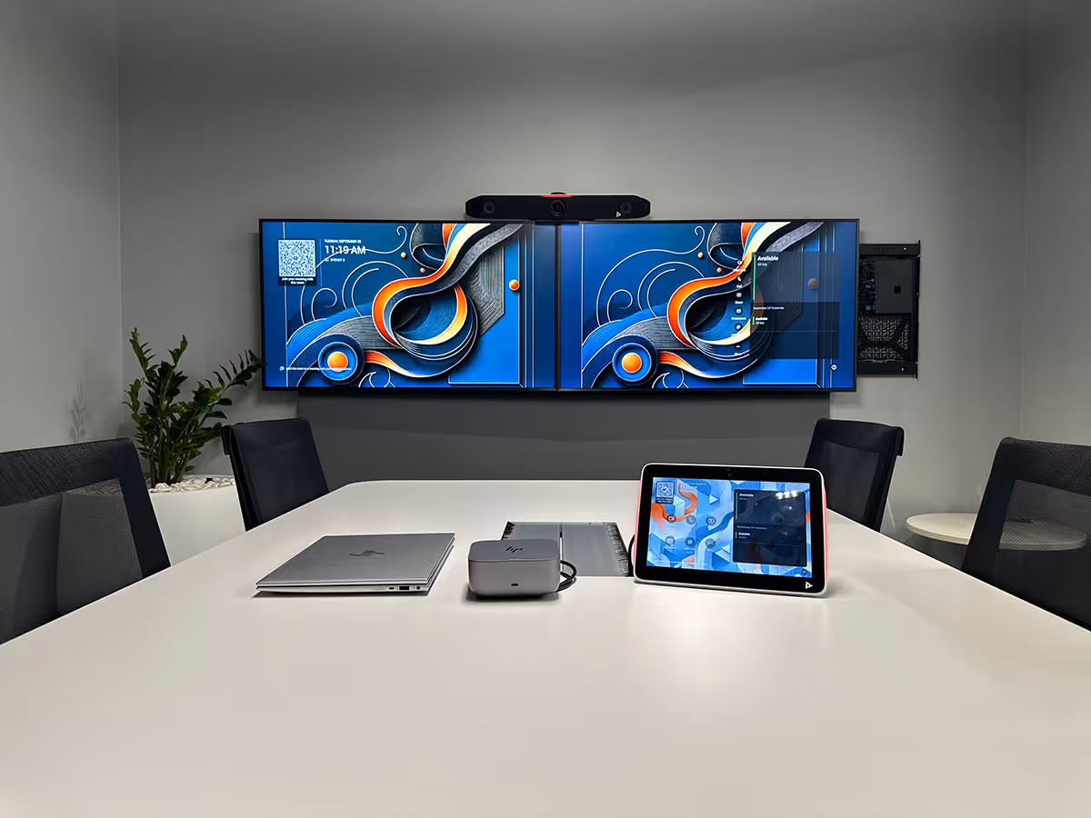 Modern meeting room with a white table, black chairs, dual wall-mounted displays, and a Poly TC10 Touch Controller on the table.