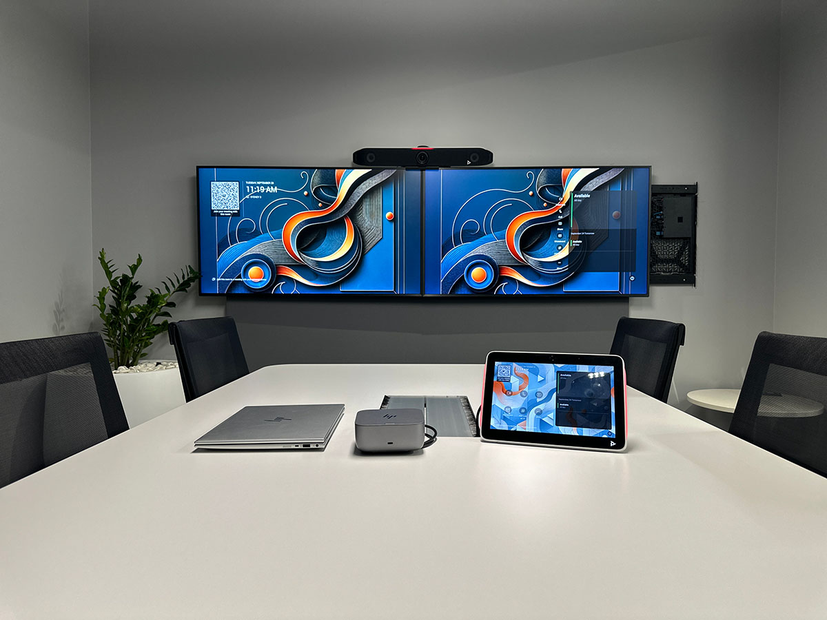 Modern meeting room with a white table, black chairs, dual wall-mounted displays, and a Poly TC10 Touch Controller on the table.