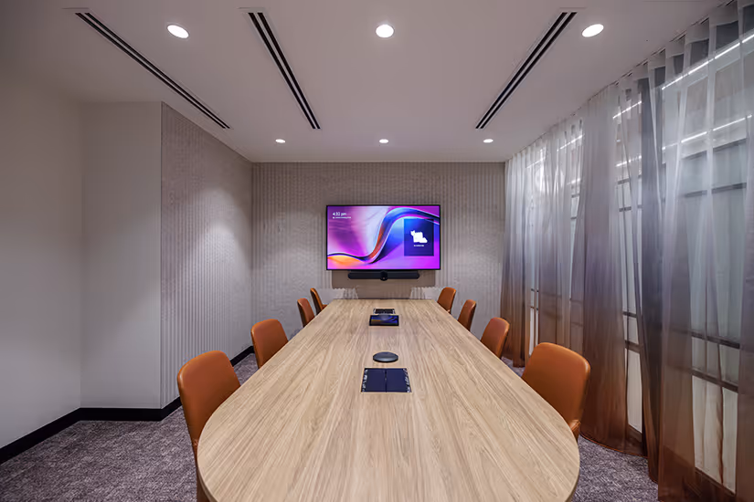 Modern conference room for Key Pharmaceuticals with a long wooden table, orange chairs, a wall-mounted TV screen, and sheer brown curtains on windows.