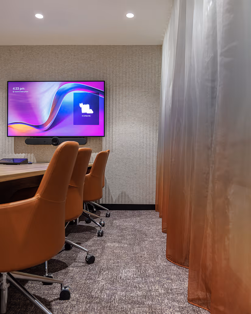 Modern conference room for Key Pharmaceuticals with brown leather swivel chairs, a long wood table, and a wall-mounted TV displaying meeting information.