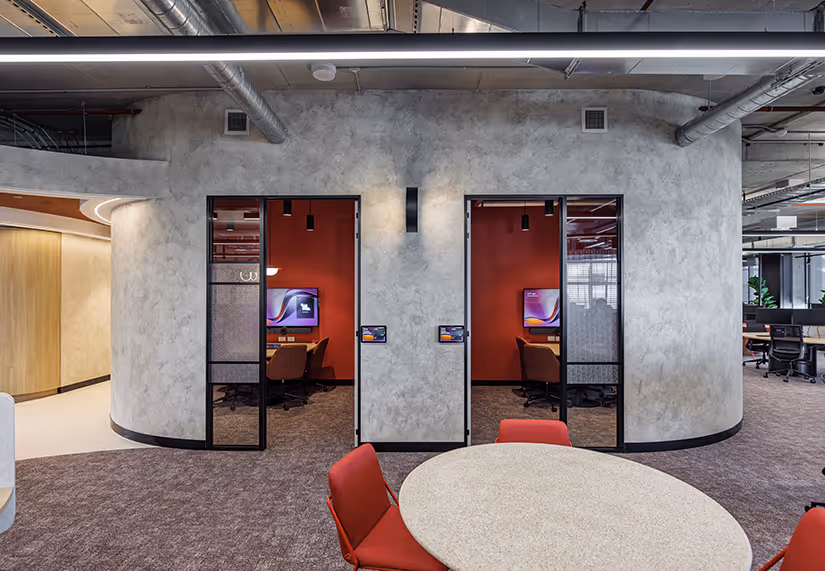 Modern office space for Key Pharmaceuticals with two small glass-door meeting rooms featuring red walls, computer monitors, and brown chairs, in front of a round table with red chairs.