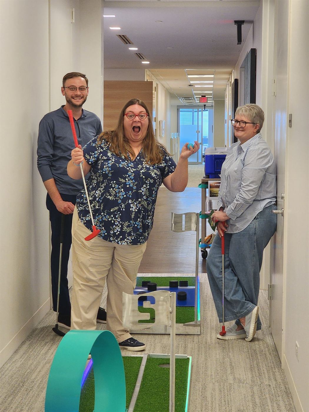 Coworkers cheering on a mini golf course set up in an office hallway