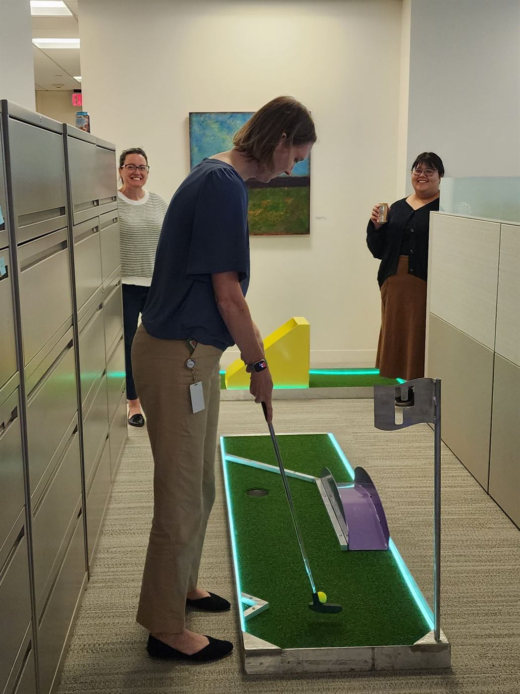 Adults putting on a glowing mini golf hole indoors