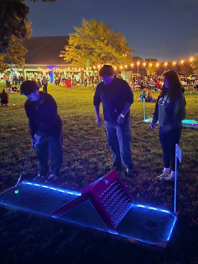 Guests playing a glowing LED mini golf hole at night