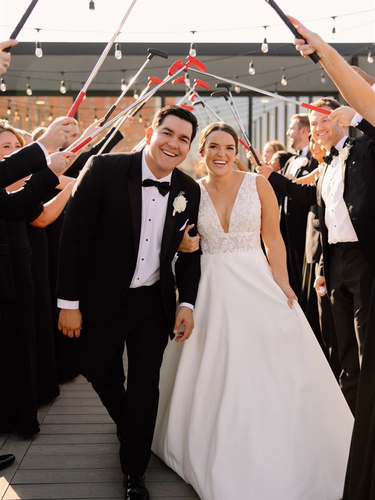 Wedding guests raising putters in an arch as the bride and groom walk through