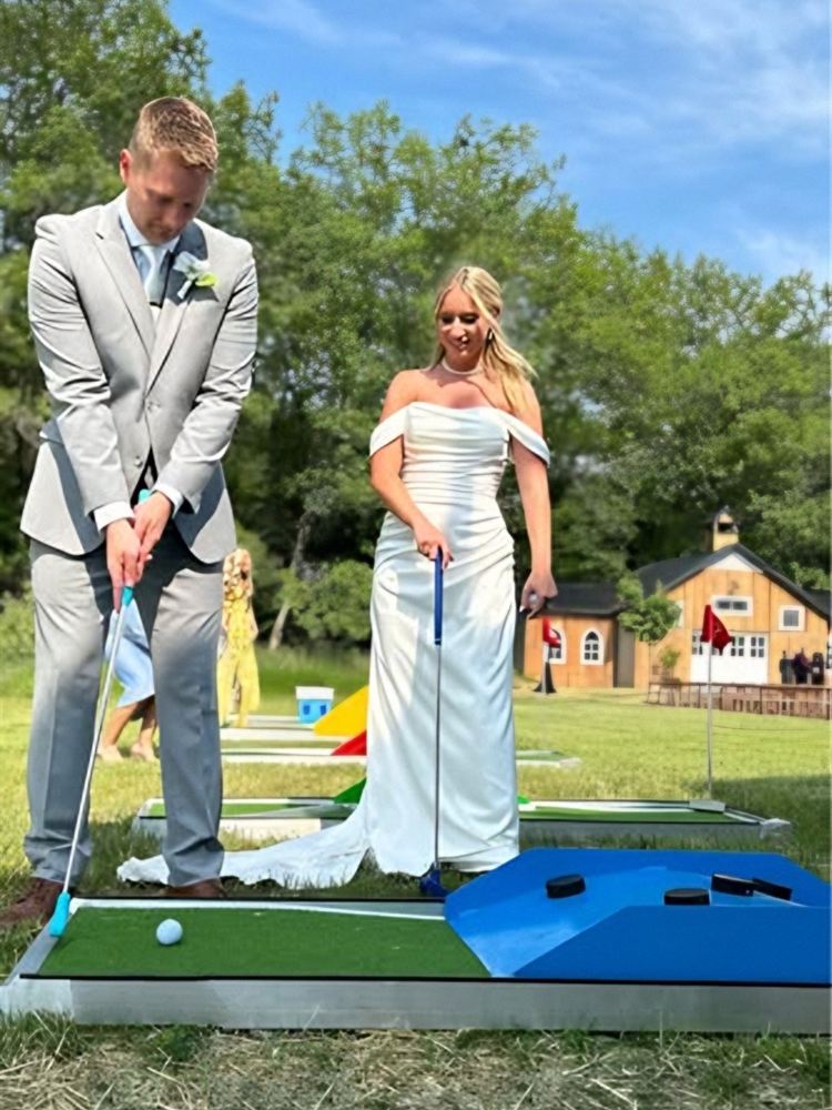 Groom putting while the bride watches on a mini golf course at an outdoor wedding