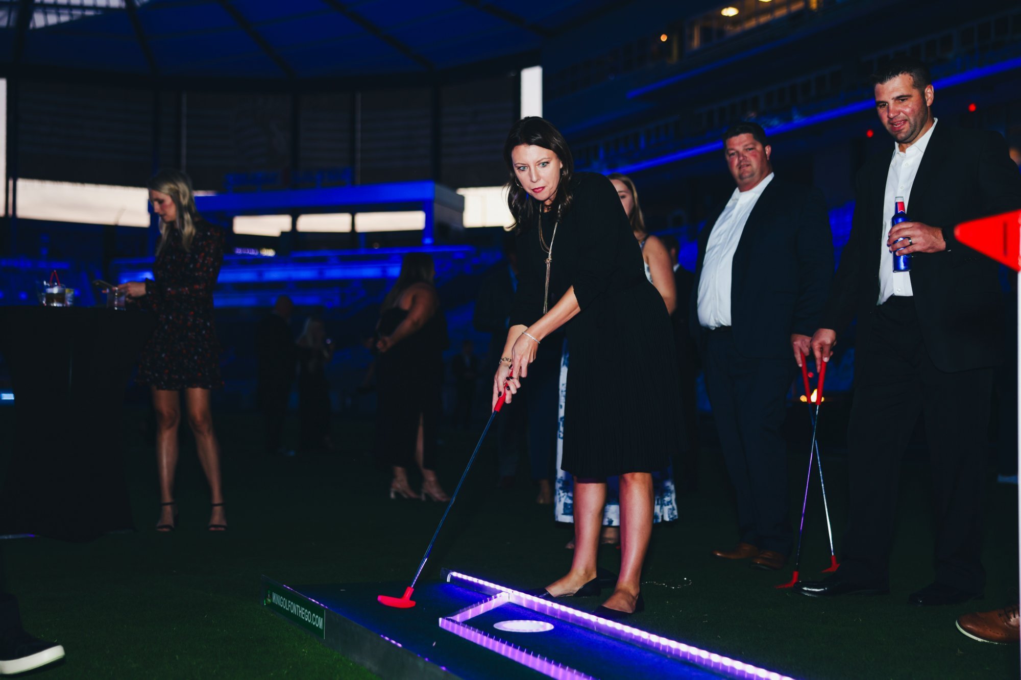 Guest in a cocktail dress putting at a nighttime corporate event in a stadium