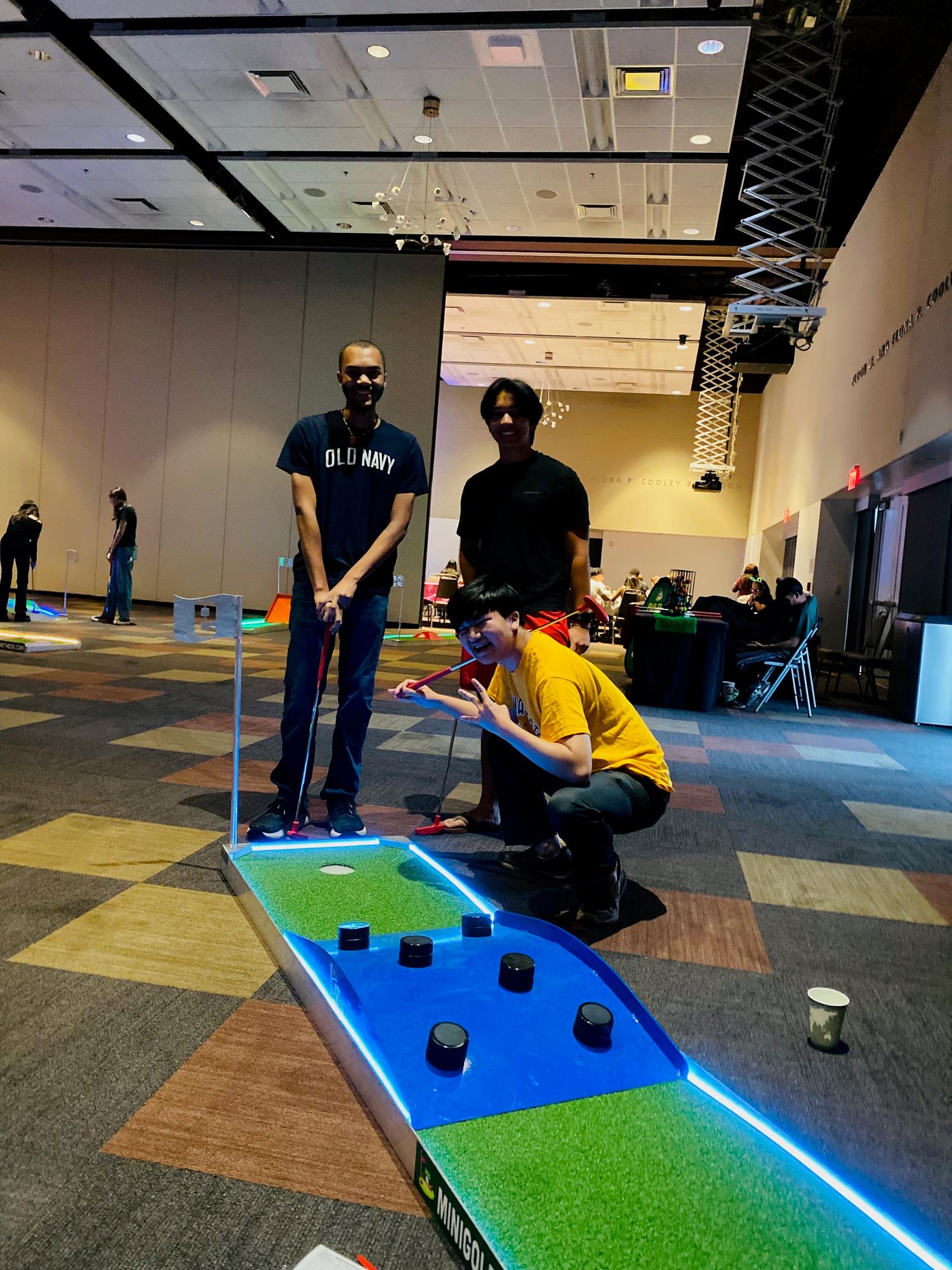 Group playing a glowing mini golf hole at an indoor ballroom event