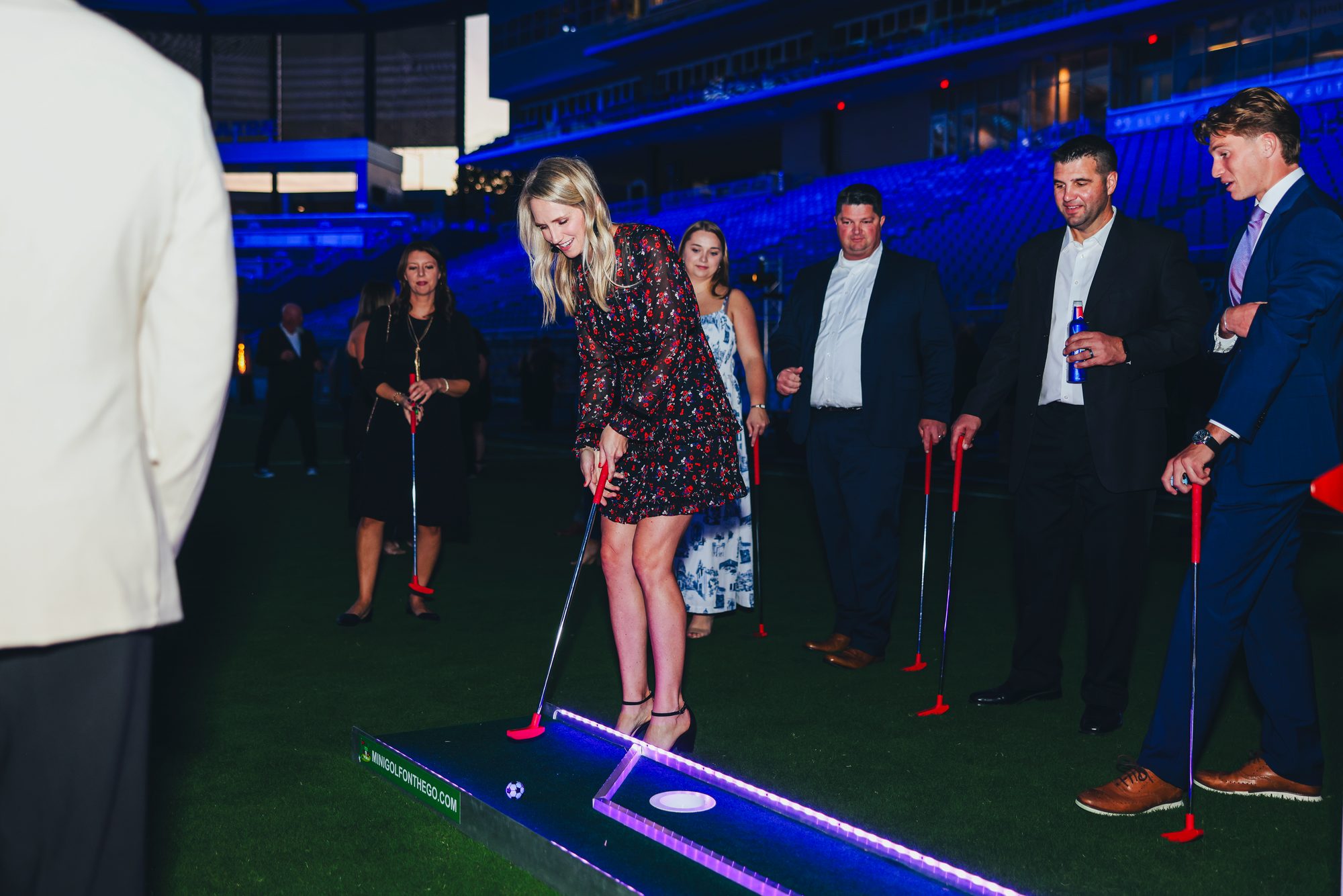 Corporate event guests putting on a glowing mini golf hole inside a stadium at night