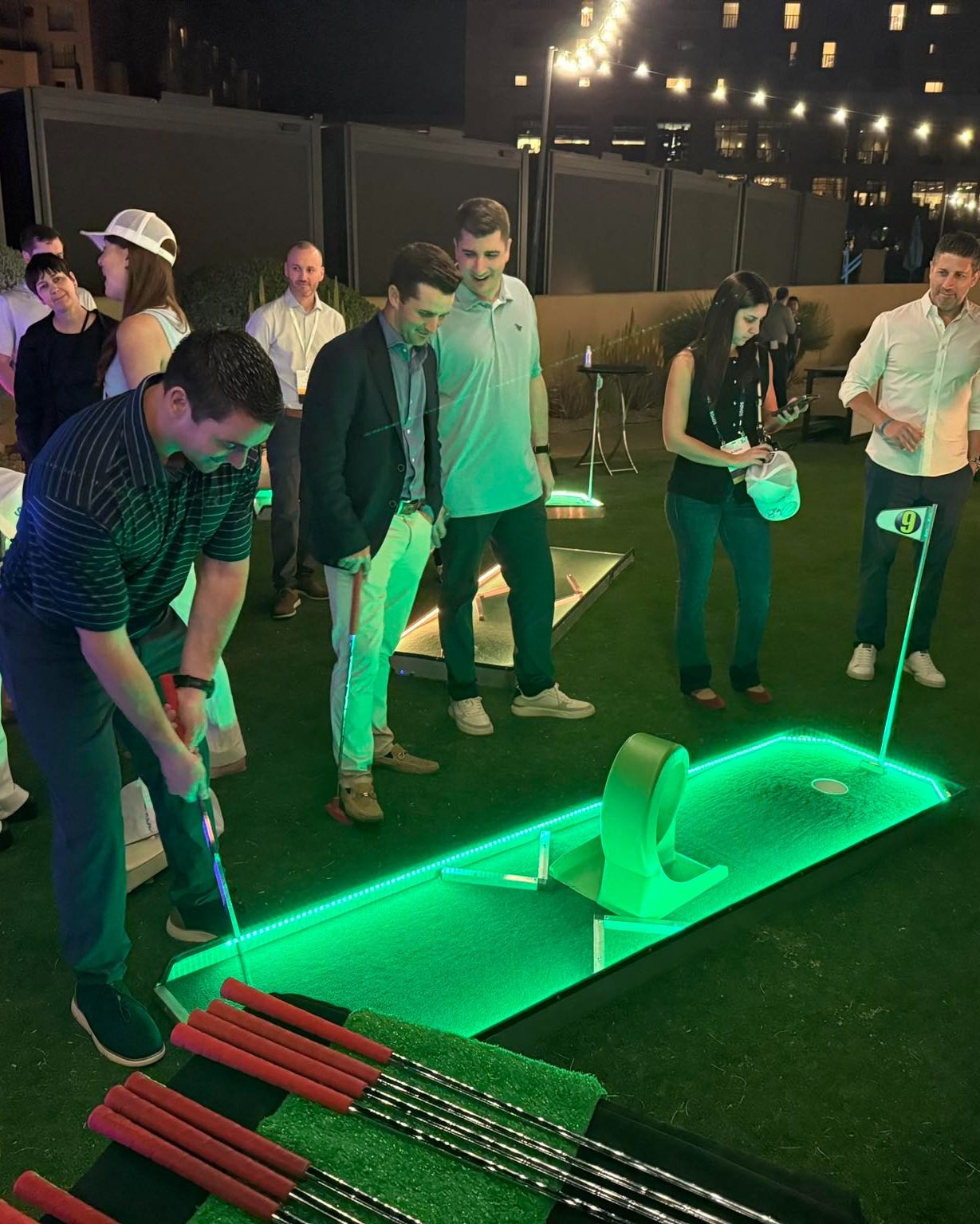 Coworkers playing a glowing mini golf course at a rooftop party at night