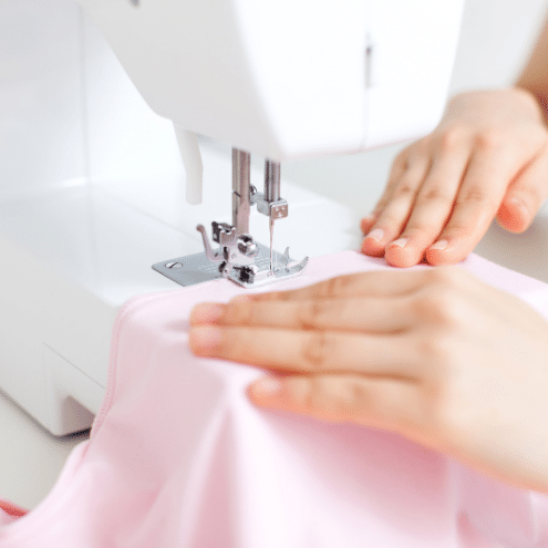A student in TaF.t's Basic Drafting and Sewing class sewing on a white domestic machine with light pink fabric.
