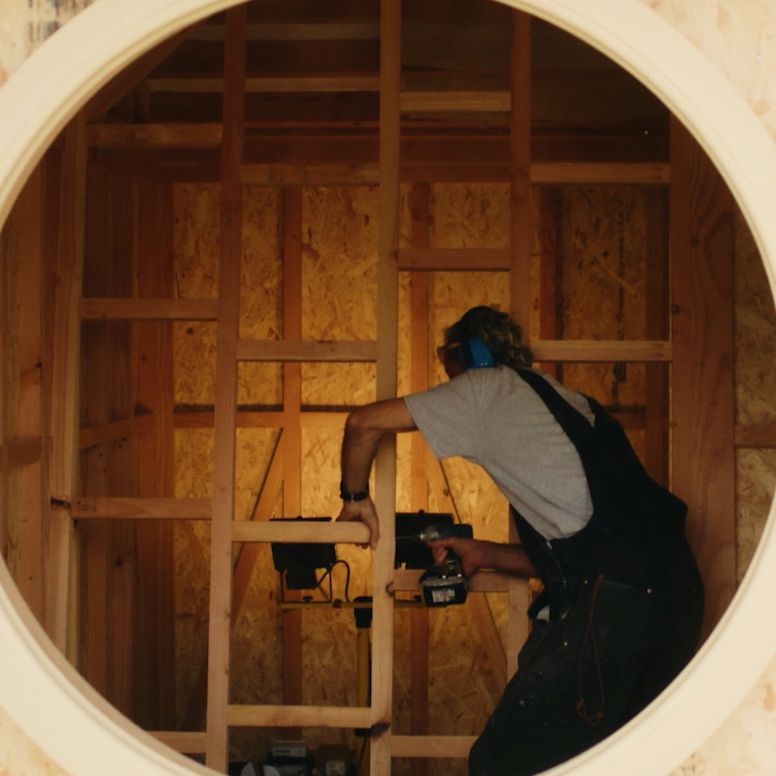 Sam Ludgate Bloom working on sauna seen through circular window