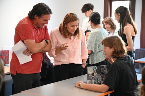 Two adults looking at a student showing their project work on their laptop