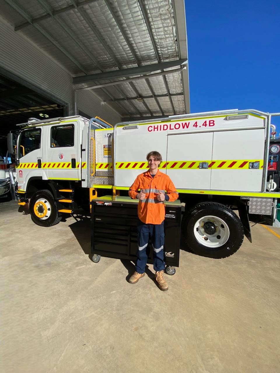 A student stood in hi-vis gear in front of a tool-box and truck