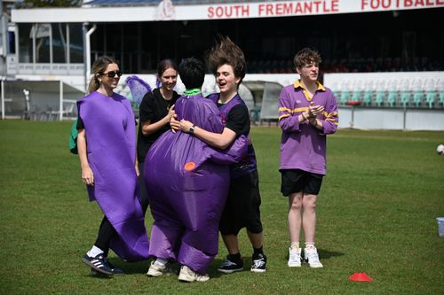 A group of students in purple fancy dress costumes hugging and jumping for joy