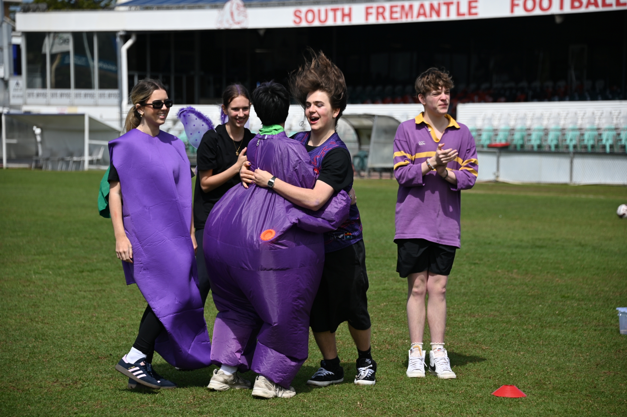 A group of students in purple fancy dress costumes hugging and jumping for joy