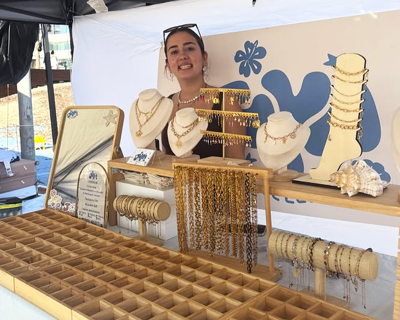 Young female entrepreneur stood behind a jewellery stall at a market