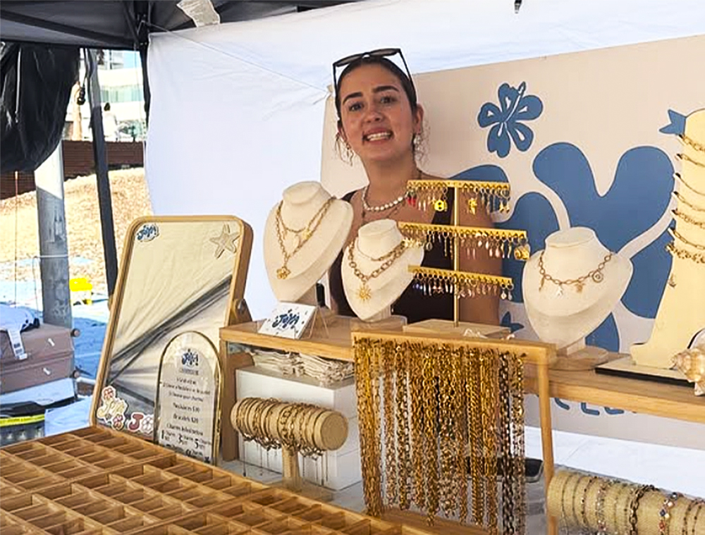 Young female entrepreneur stood behind a jewellery stall at a market
