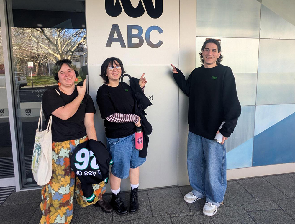 Three students stood outside the ABC Radio station building pointing at the logo