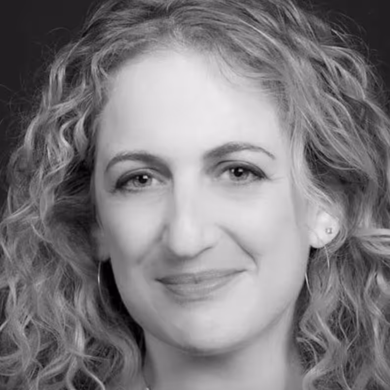 Close-up black-and-white portrait of a woman with curly hair smiling softly against a dark background.