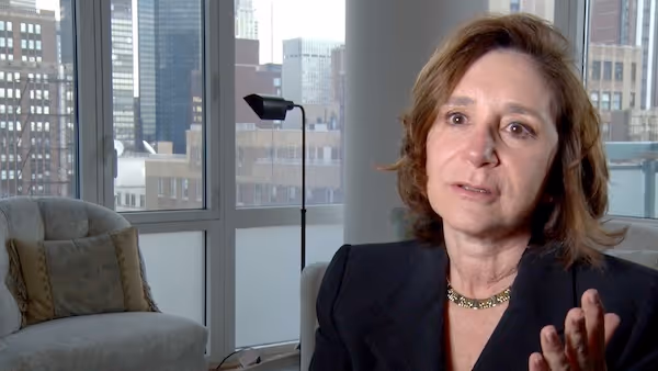Sherry Turkle speaking to camera against a city backdrop out of the window behind her