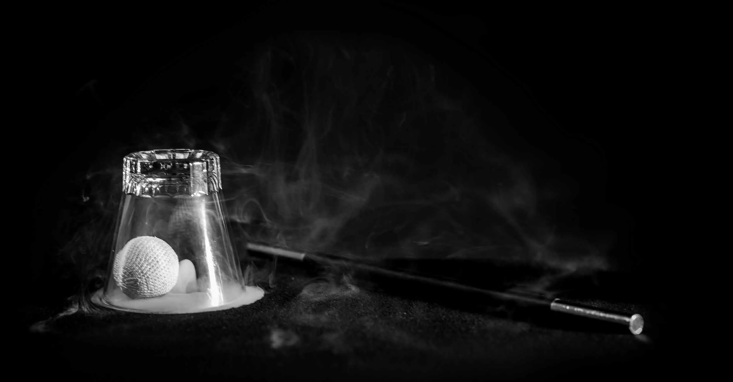 Foto på trollstav och ett rökfyllt glas med en vit boll i. Från Jacob Schenströms Cups & Balls.