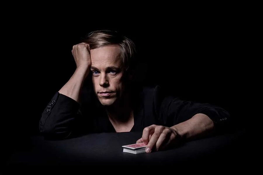 Jacob Schenström is sitting at a table with a deck of cards in one hand.