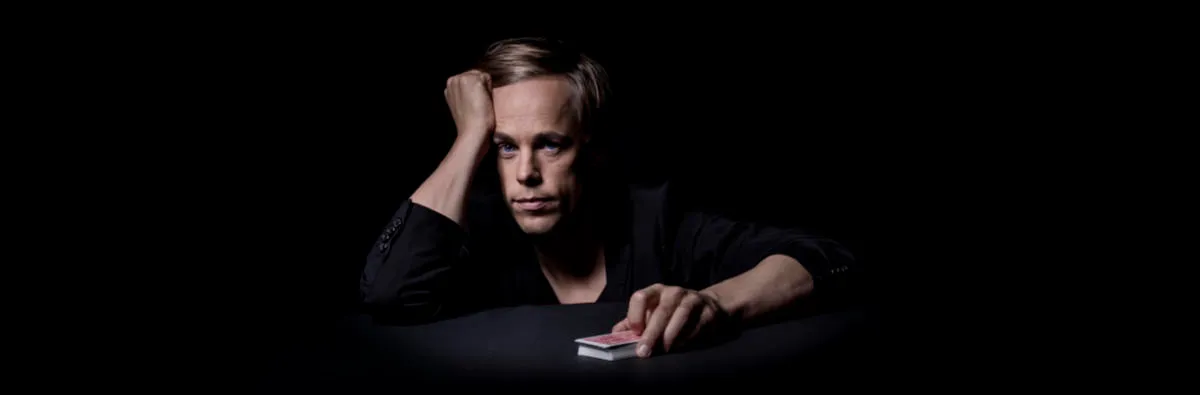 Jacob Schenström is sitting at a table with a deck of cards in one hand.