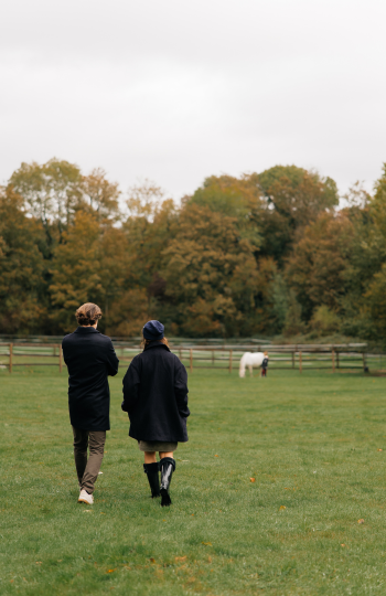A man and a woman are walking around the Maffliers estate, watching the horses in the distance.
