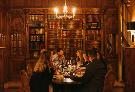 A group of friends enjoy a delicious dinner in a magnificent wood-paneled dining room at the Augustine restaurant in the Château de Maffliers.