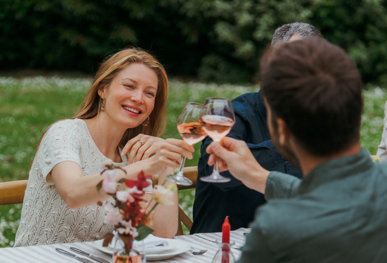 Un homme et une emme trinque avec deux verres de rosé, sur une belle table champêtre au milieu d'une clarirrière.