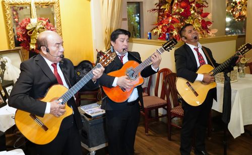 Three men stand side by side in a restaurant, playing guitar and singing.
