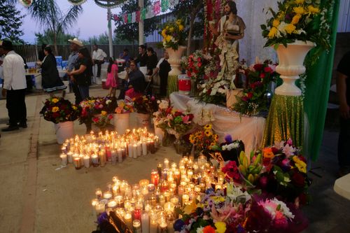An altar with the statue of San Juan Bautista covered in flowers and money. Candles are lined up at the foot of the altar.