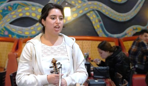 Xóchitl Morales, a young woman, sings while holding a violin relaxedly in both hands.