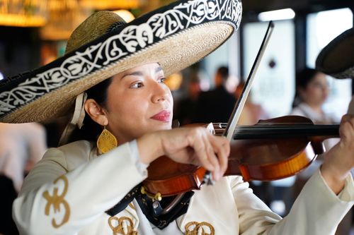 A close-up of Marilyn Rodriguez, a woman mariachi wearing a sombrero, playing a violin.