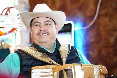A man in a white hat smiles, holding an accordion.