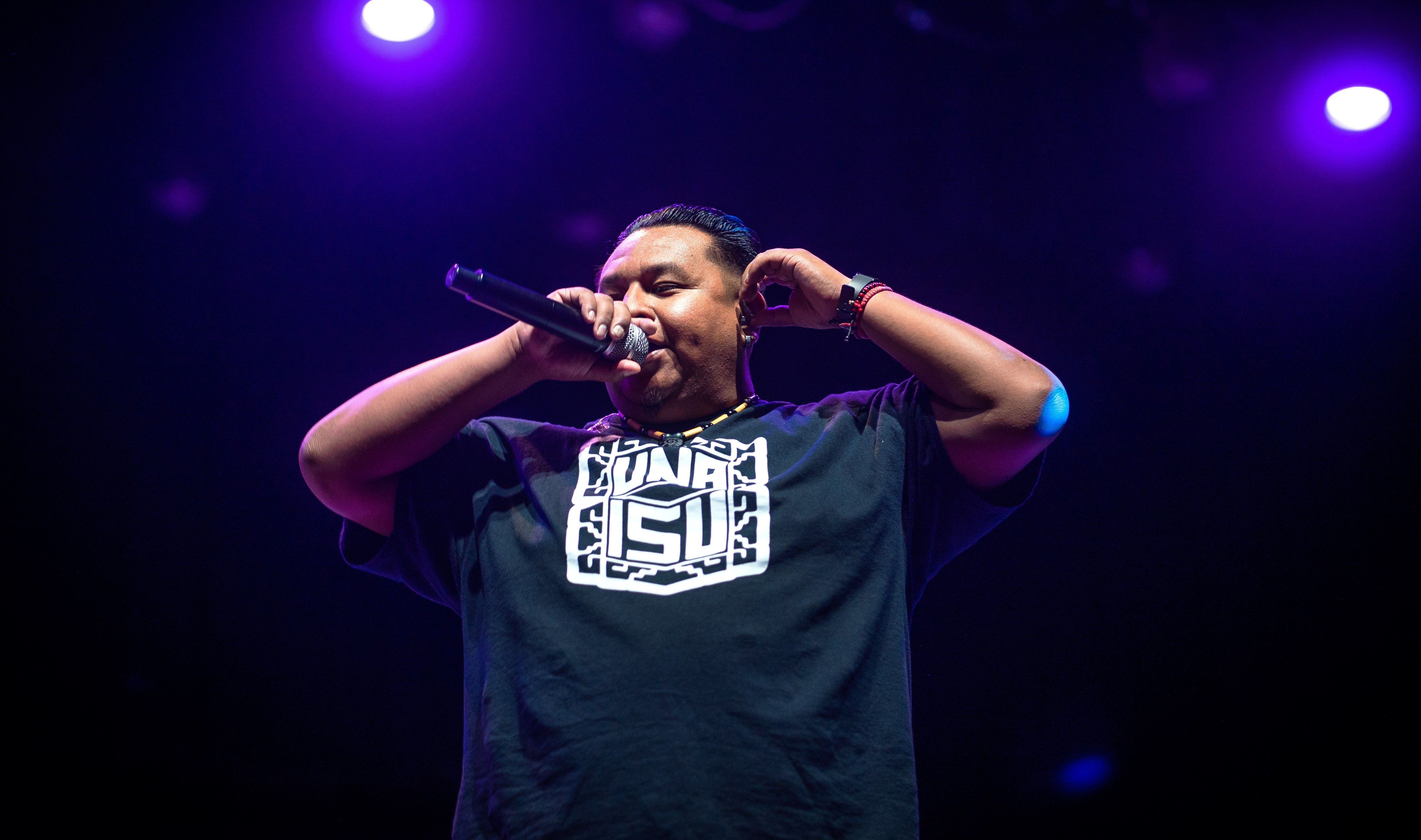 A photo taken from a low angle of a man in a black t-shirt performing beneath blue stage lights.