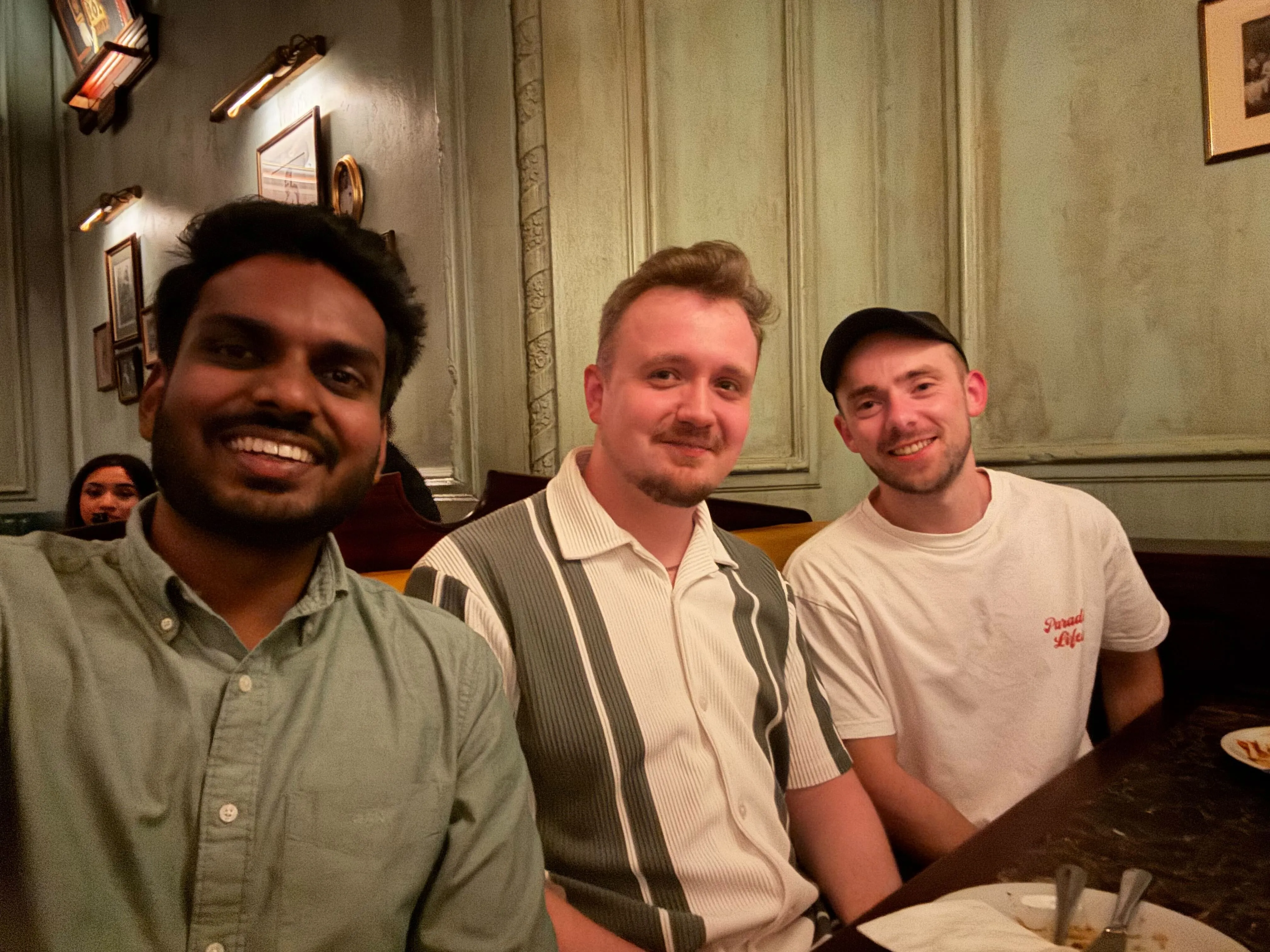 Three men sitting closely together at a restaurant table smiling at the camera.